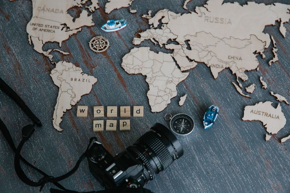 A creative flat lay of a wooden world map, camera, and compass.