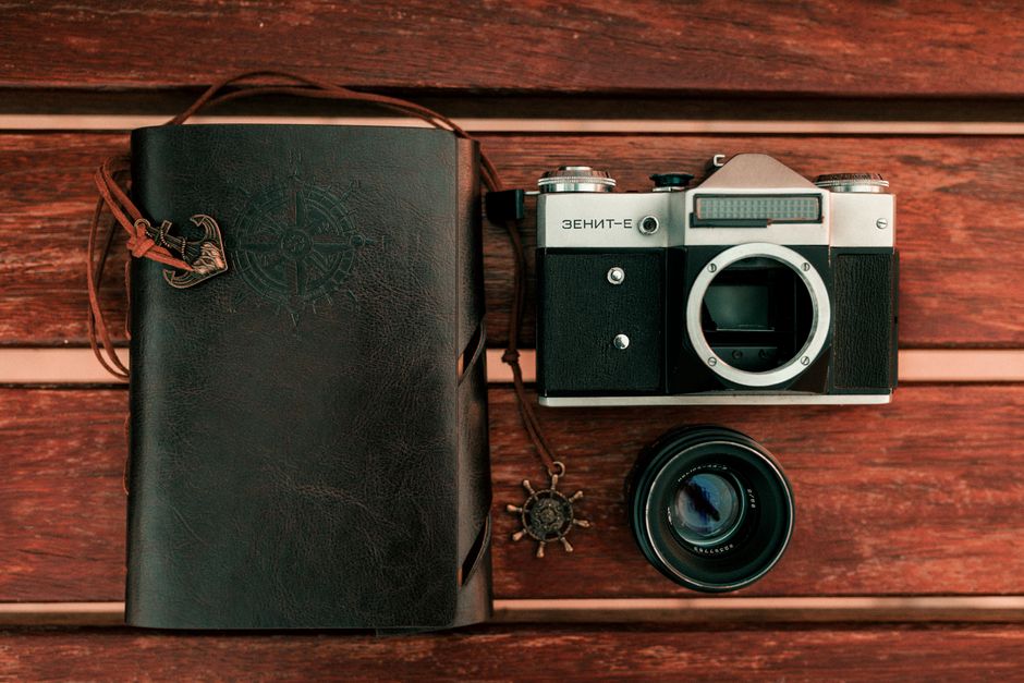 A classic vintage camera and leather journal laid on a wooden table, evoking nostalgia and adventure.