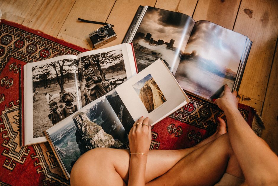 Person browsing photography books on a vintage rug with an analog camera in view.