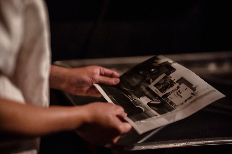 A person examines a freshly developed black-and-white photo in a dimly lit darkroom.